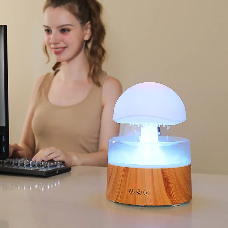 White cloud-shaped humidifier with falling raindrop mist and multi-colour night light on wooden table