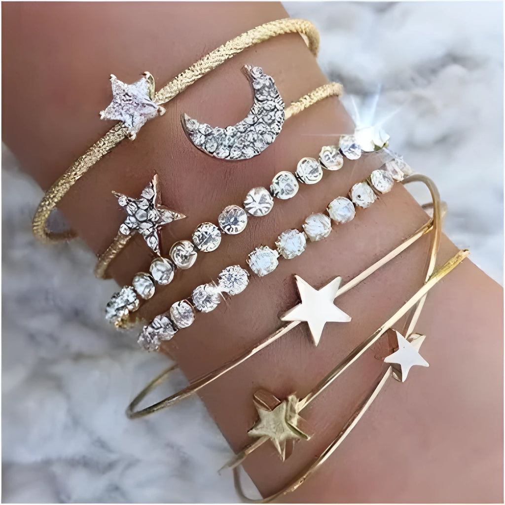 Four gold and silver metal cuff bracelets with moon and star designs on a plain background