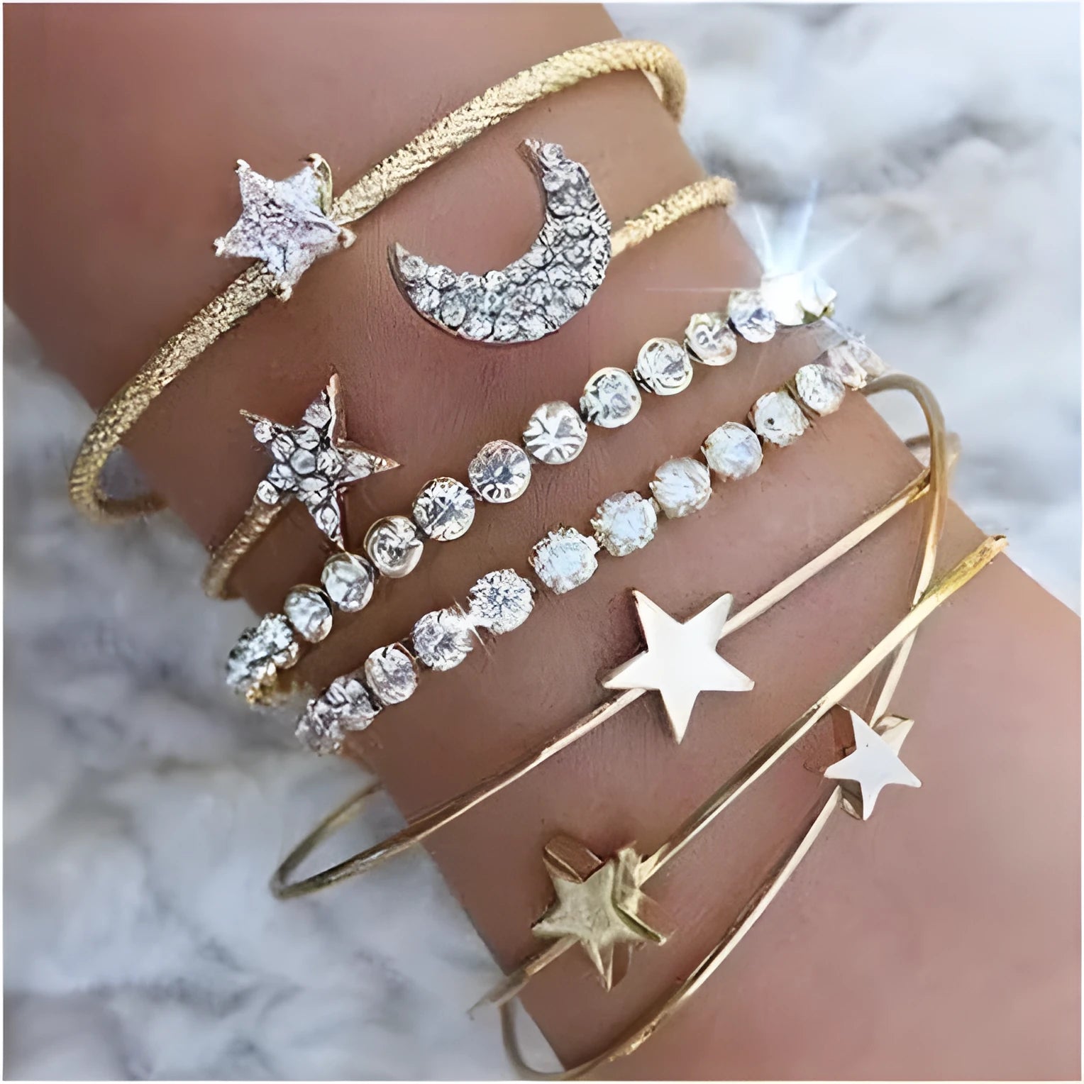 Four gold and silver metal cuff bracelets with moon and star designs on a plain background