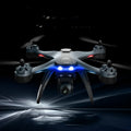 Plastic quadrocopter drone with four rotors, a handheld remote controller, and spare fan blades on a landing gear.