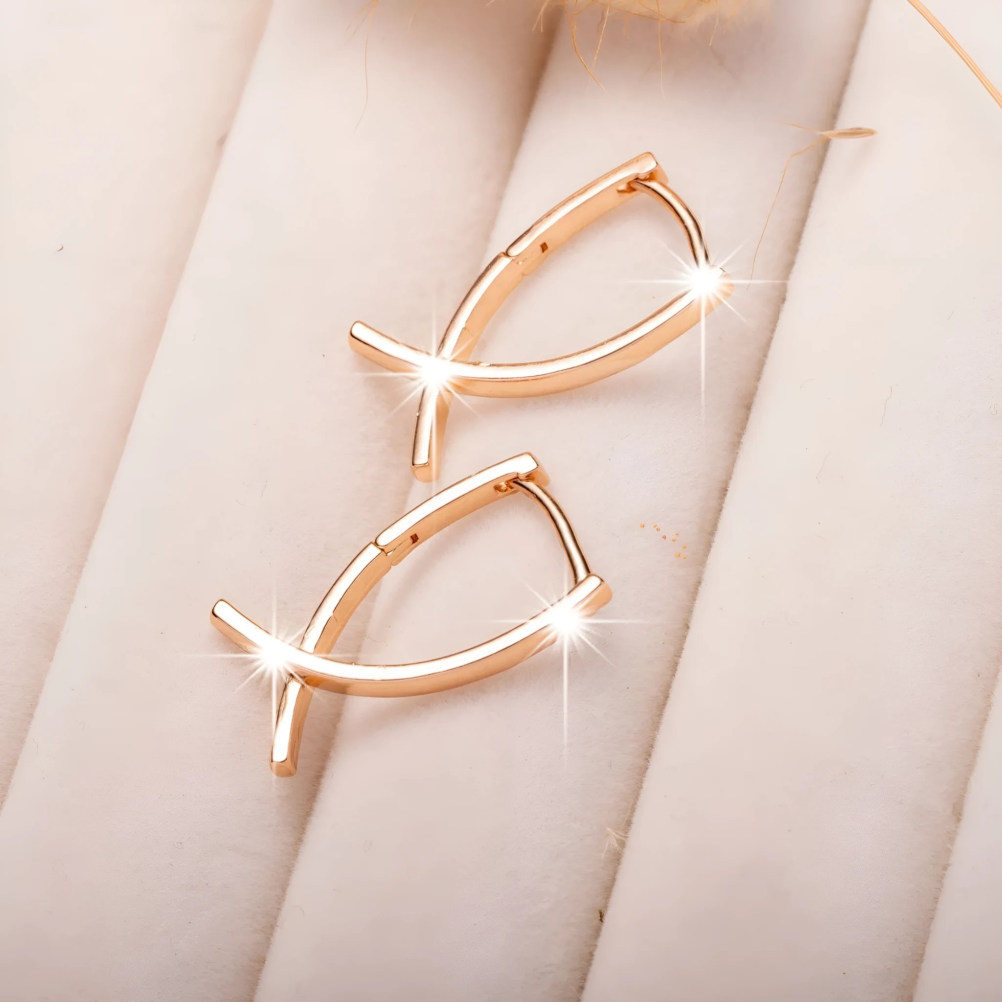 A pair of rose gold coloured cross pendant earrings on a copper base.