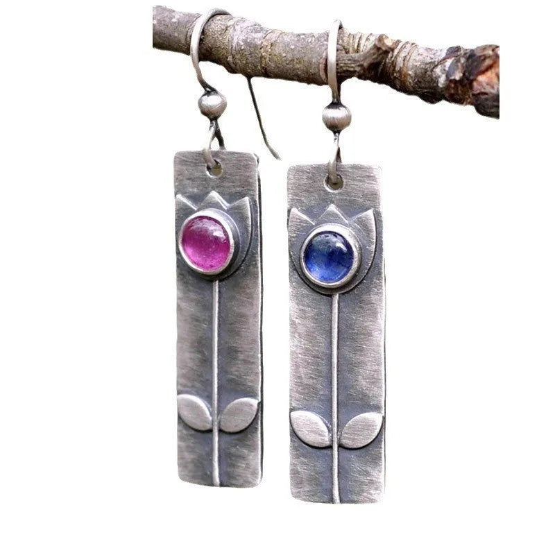 Antique finish red sapphire earrings with geometric shape and elliptical gemstone elements on metal background