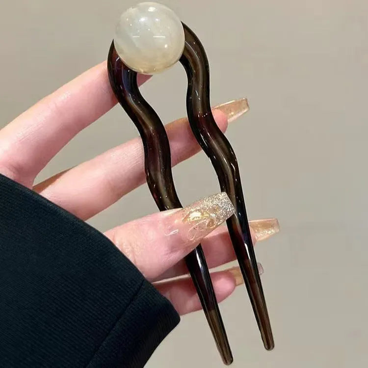 Acrylic U-shaped hair barrette with a small spherical decoration in a beige and caramel two-tone colour combination.