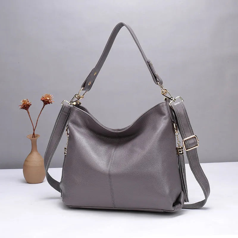 A vertical square-shaped genuine leather crossbody bag in black, showing external sewing lines and a crossbody strap.