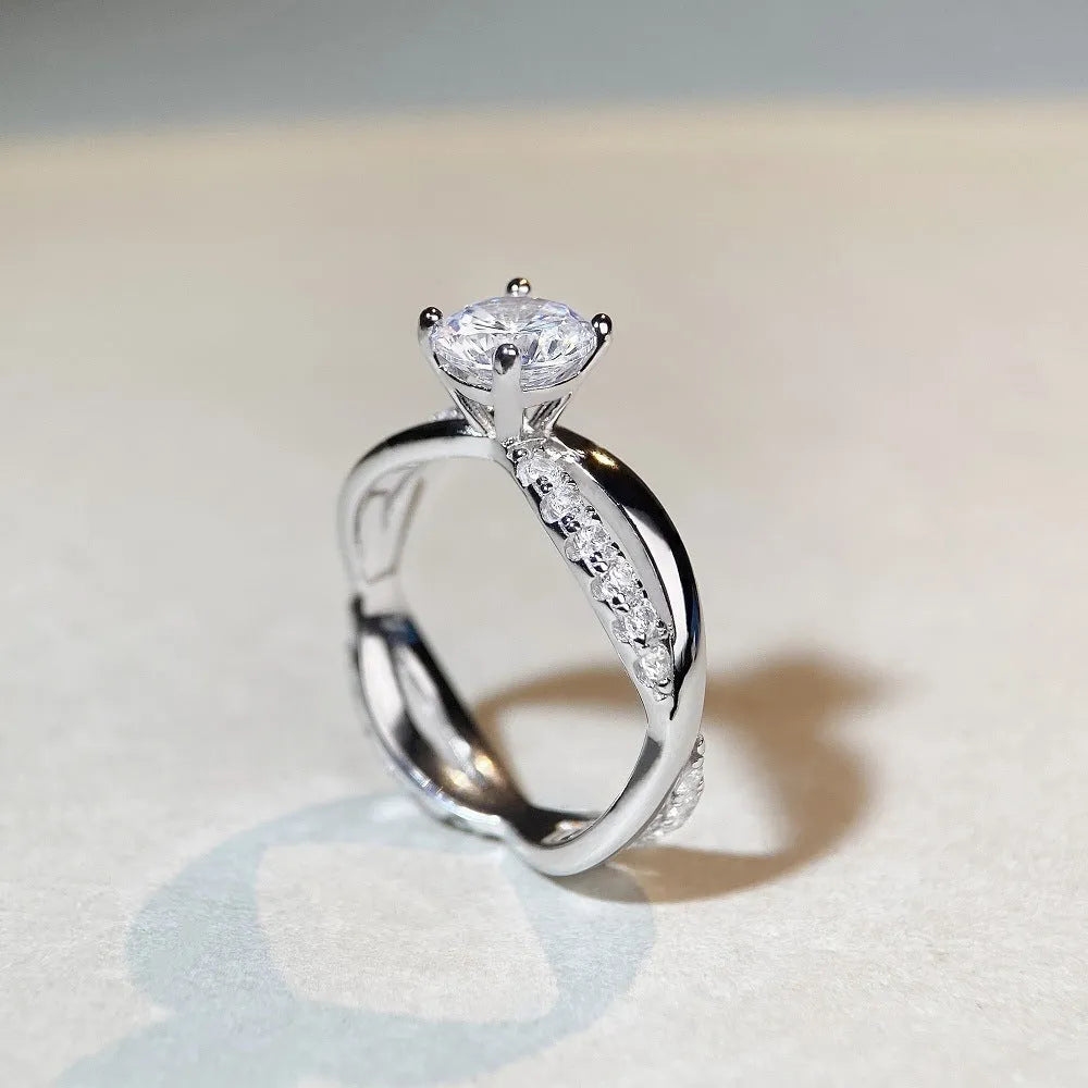 Geometric silver ring with a 1 karat moissanite in a four-claw setting, showing twisted band and cross design.