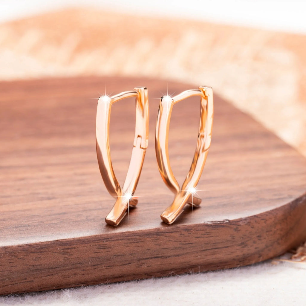 A pair of rose gold coloured cross pendant earrings on a copper base.