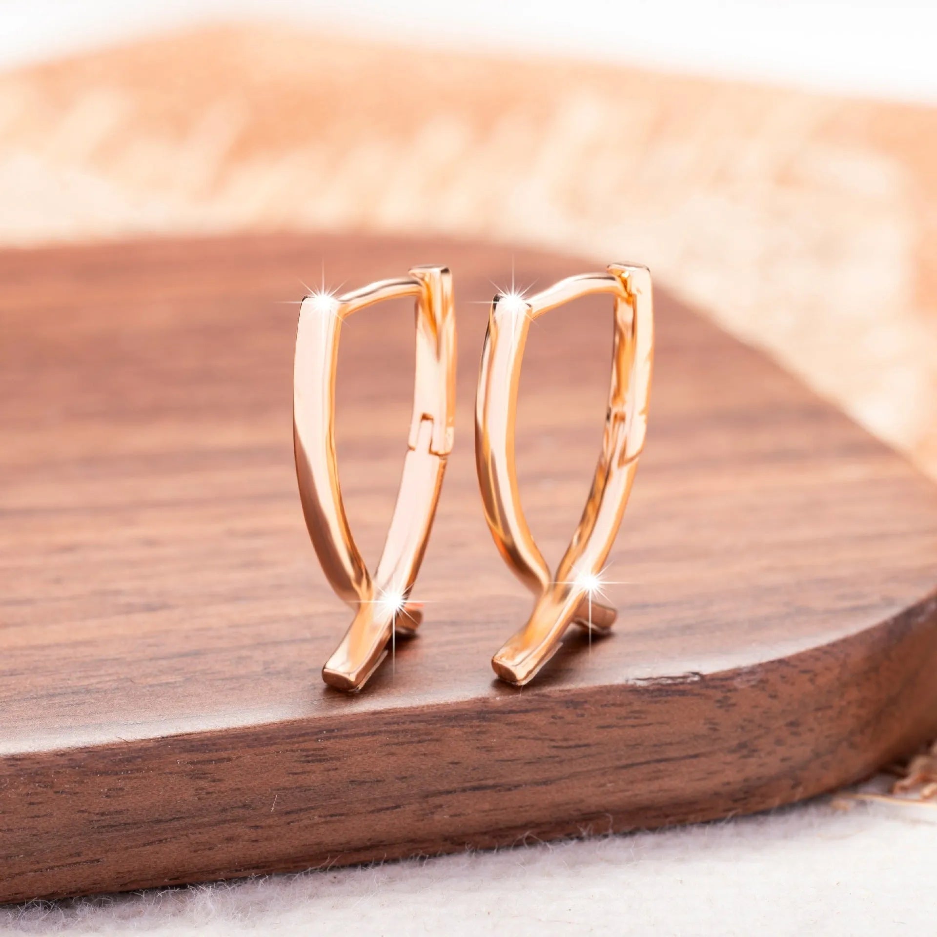 A pair of rose gold coloured cross pendant earrings on a copper base.