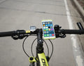 A black silicone bicycle phone holder mounted on a bike handlebar, showing the three adjustment holes and buckle fastener.