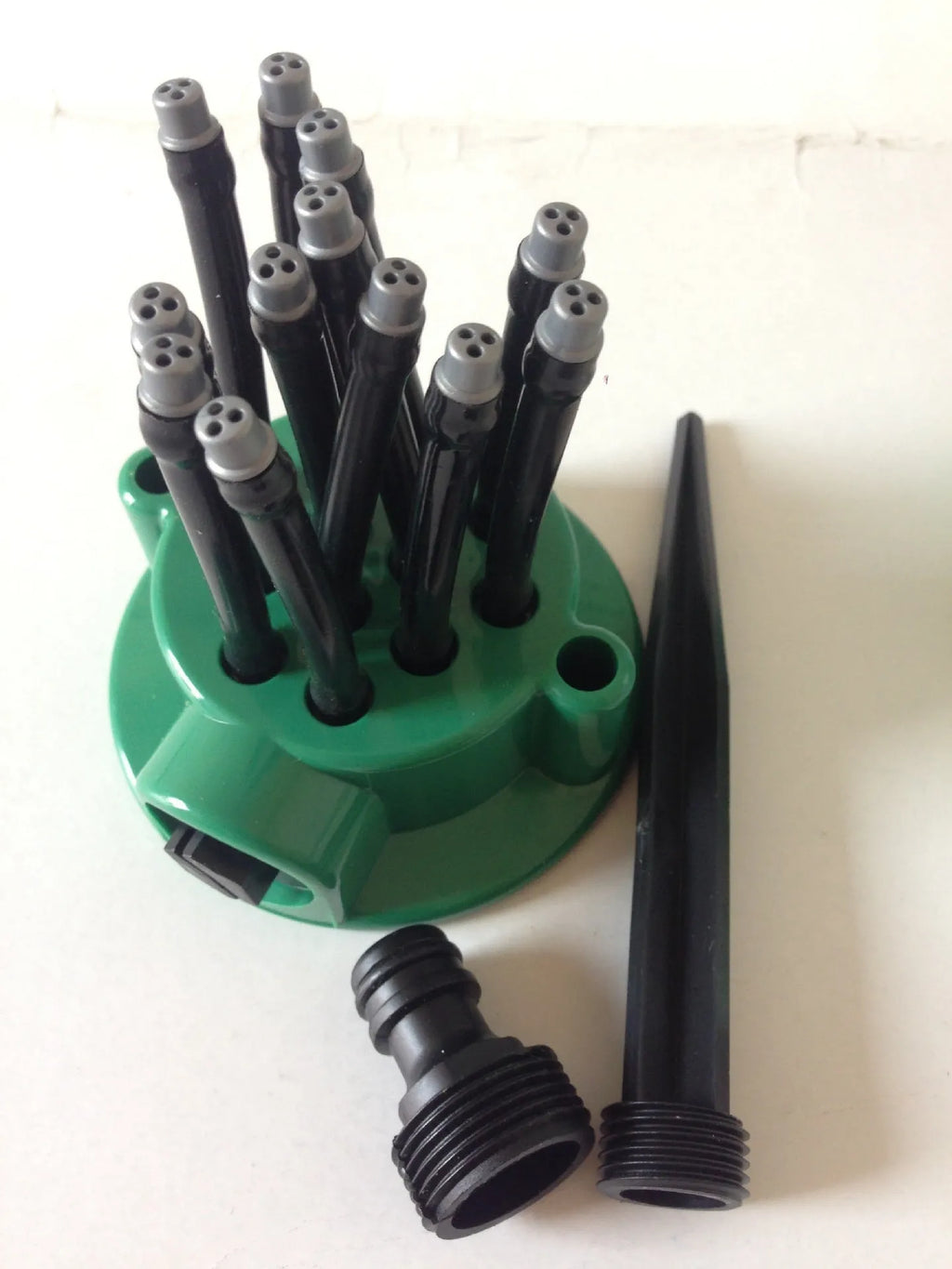 Green adjustable lawn sprinkler with bendable plastic nozzles on circular base