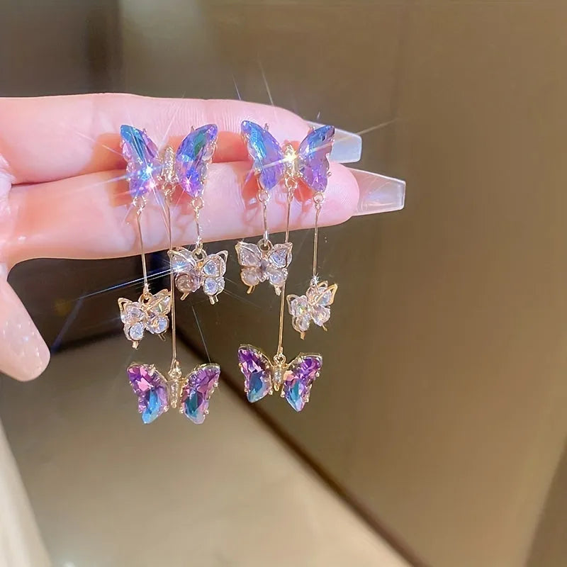 Women's silver needle coloured drop earrings with purple butterfly charm, crystal flowers, and tassels.