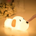 Soft silicone cartoon dog night light with USB cable on a bedside table.