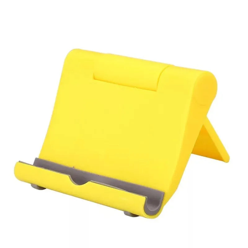 Black foldable PE plastic phone and tablet stand on a desktop, showing adjustable viewing angles.