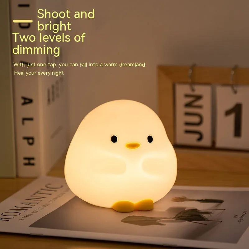 Cute duck shaped LED night lamp with silicone casing and warm light on a bedside table