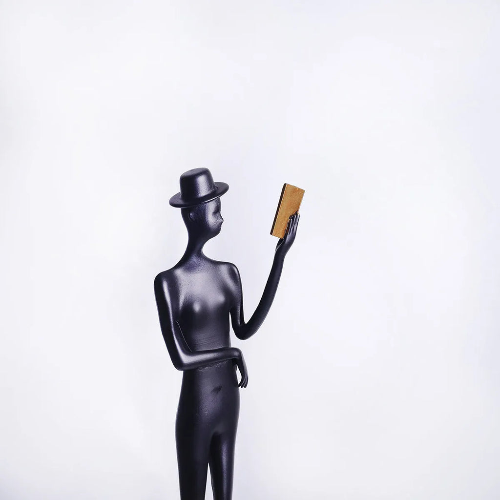 Black metal sculpture of a woman reading, modern aluminium desktop ornament.