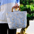 Light blue square canvas shoulder bag with bronzing flower detail and double strap connectors