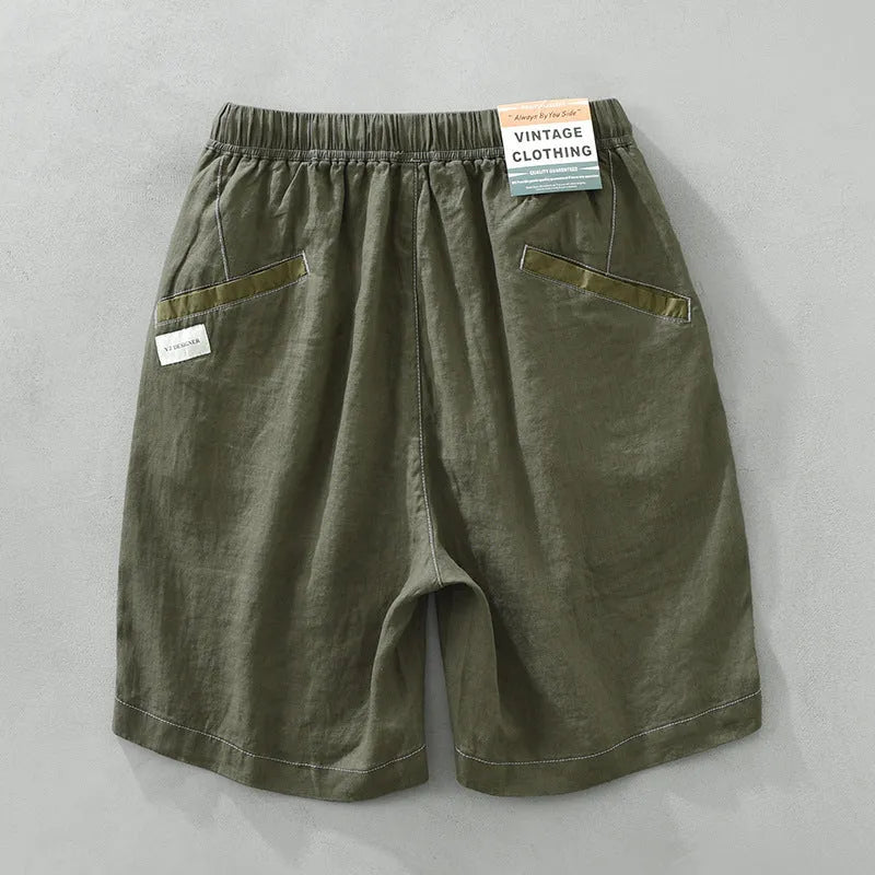 Man wearing green linen drooping shorts with a drawstring waist and mid-calf length.