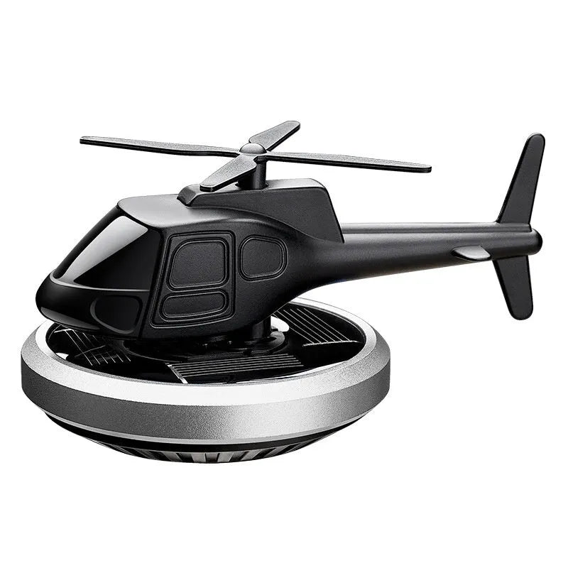 Silver metal solar-powered helicopter car ornament with rotating blades on a car dashboard.