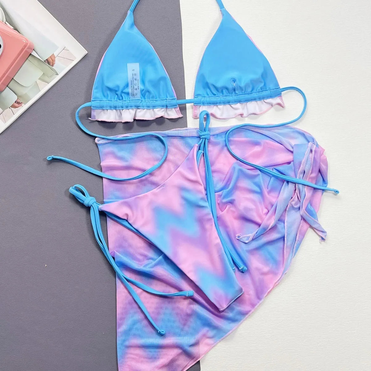 Women's tie-dye pattern bikini set with matching skirt on a neutral background.