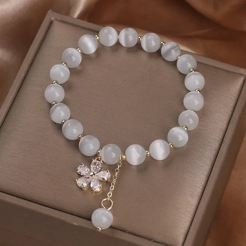 White cat's eye stone bracelet with small flower charms, tassel pendant, and safety buckle clasp.