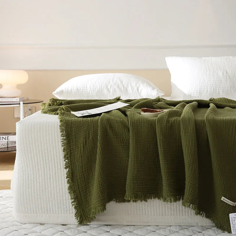 Soft cotton four-layer gauze throw blanket with tassel edges in navy blue, shown draped over a sofa.
