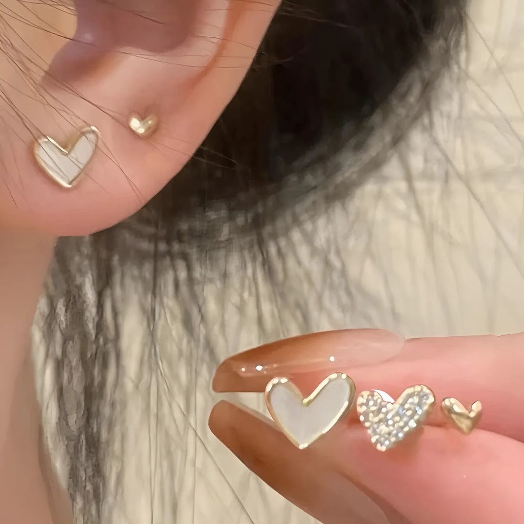 Set of three pairs of heart-shaped alloy earrings in gold, black, white, and pink colours.