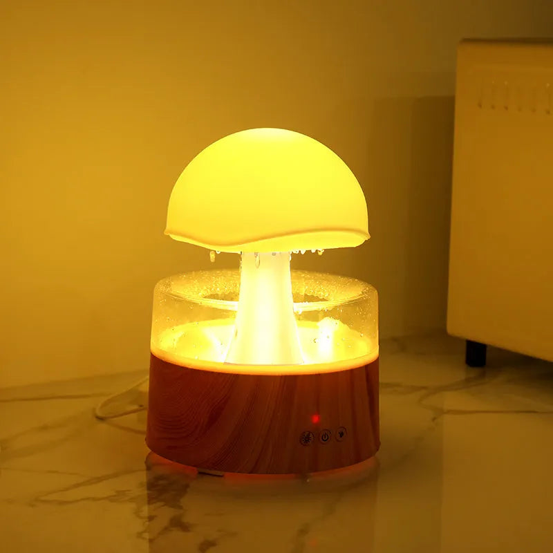 White cloud-shaped humidifier with falling raindrop mist and multi-colour night light on wooden table
