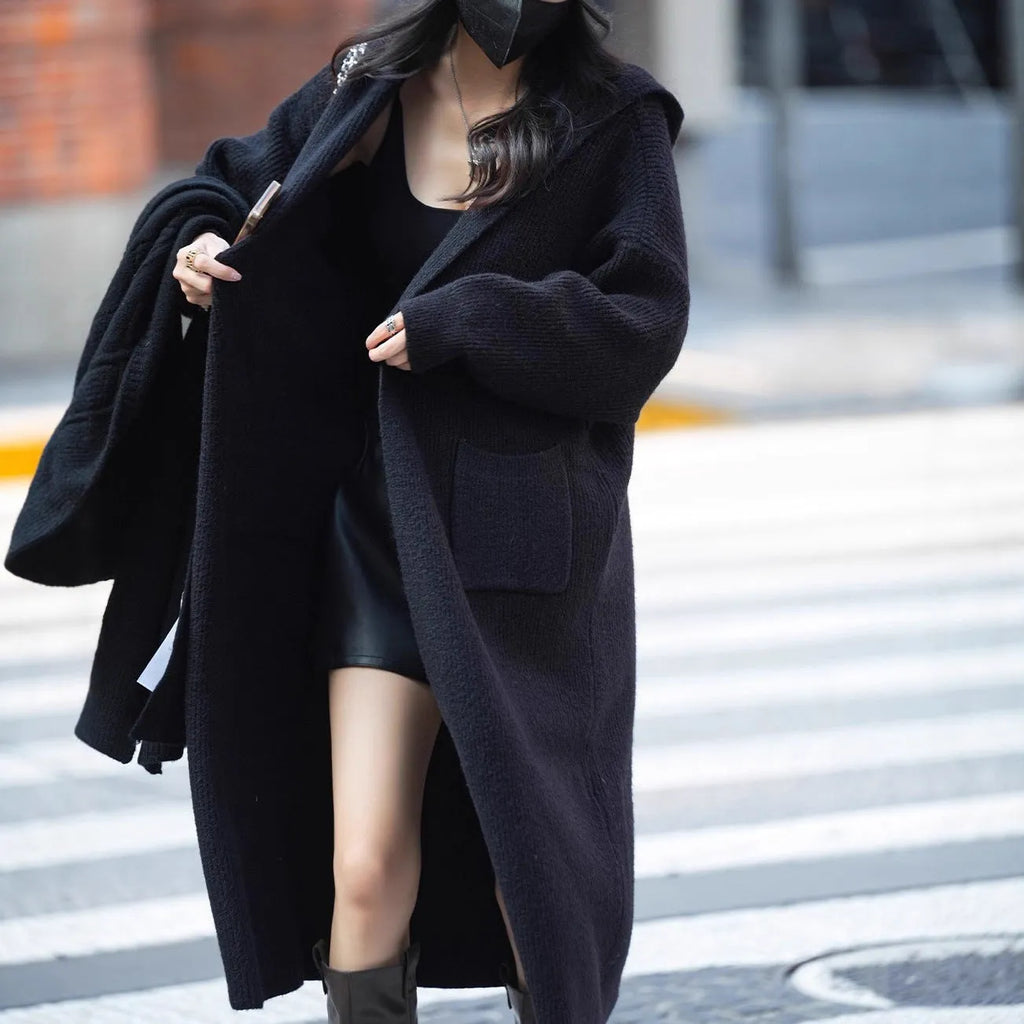 Long grey knitted women's cardigan with a hood, styled like a trench coat, on a hanger.
