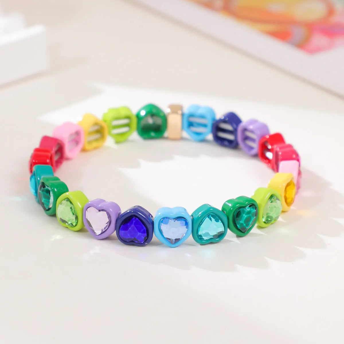 Colourful enamel finish alloy heart charm on a black stretch bracelet band.
