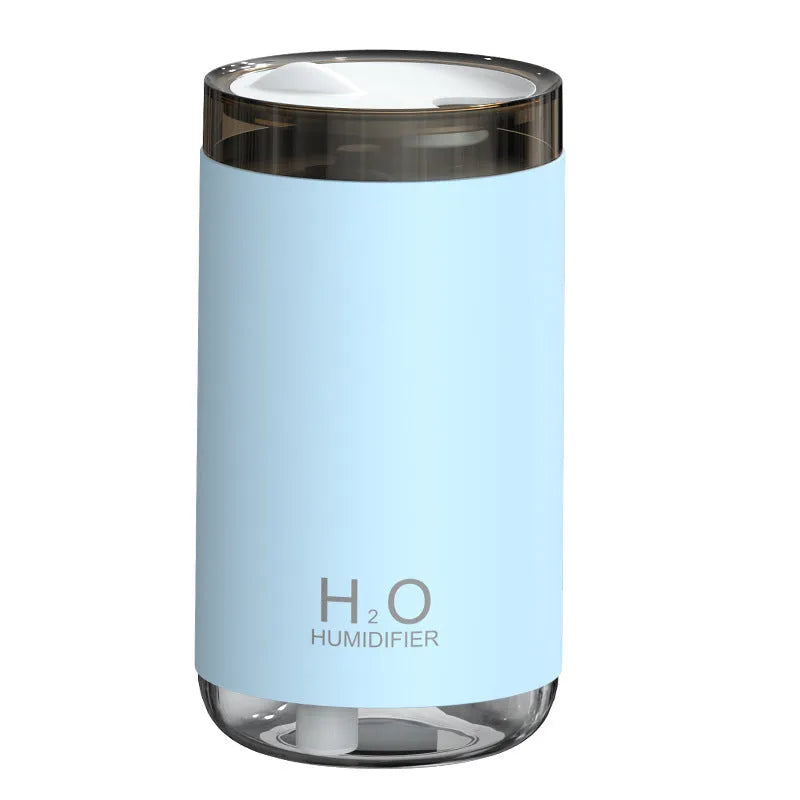 Blue jellyfish-shaped USB humidifier emitting smoke ring mist with warm night light on, placed on a wooden desk.