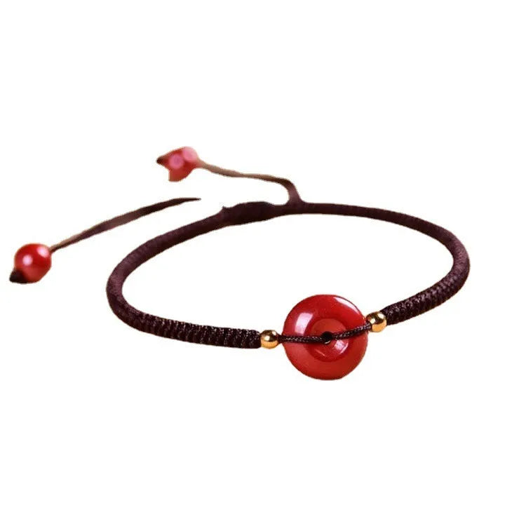Close-up of a cinnabar heart charm on an adjustable black rope bracelet with a safety buckle.