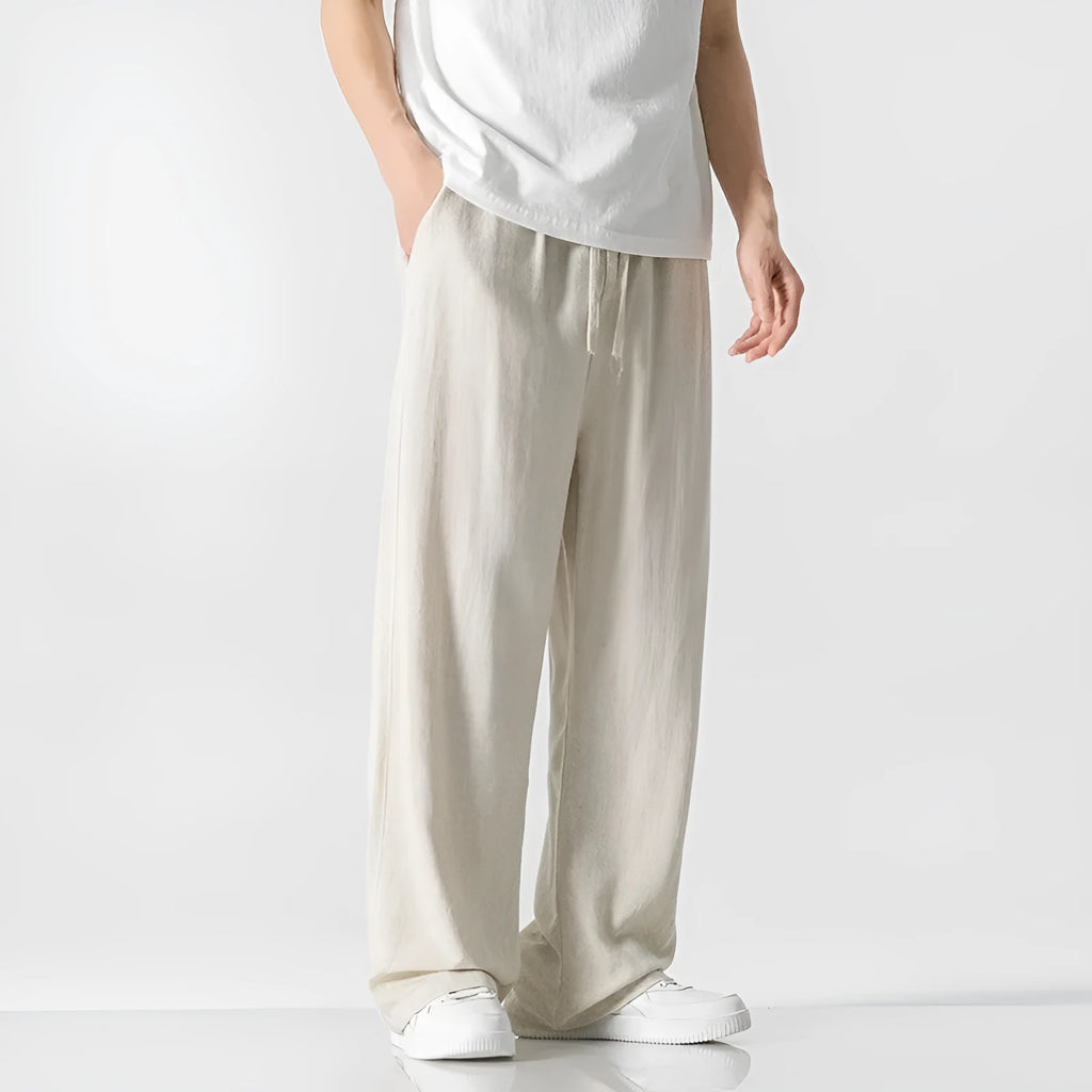 Man wearing beige straight-leg linen trousers with a drawstring waist, showcasing the cropped length and casual fit.