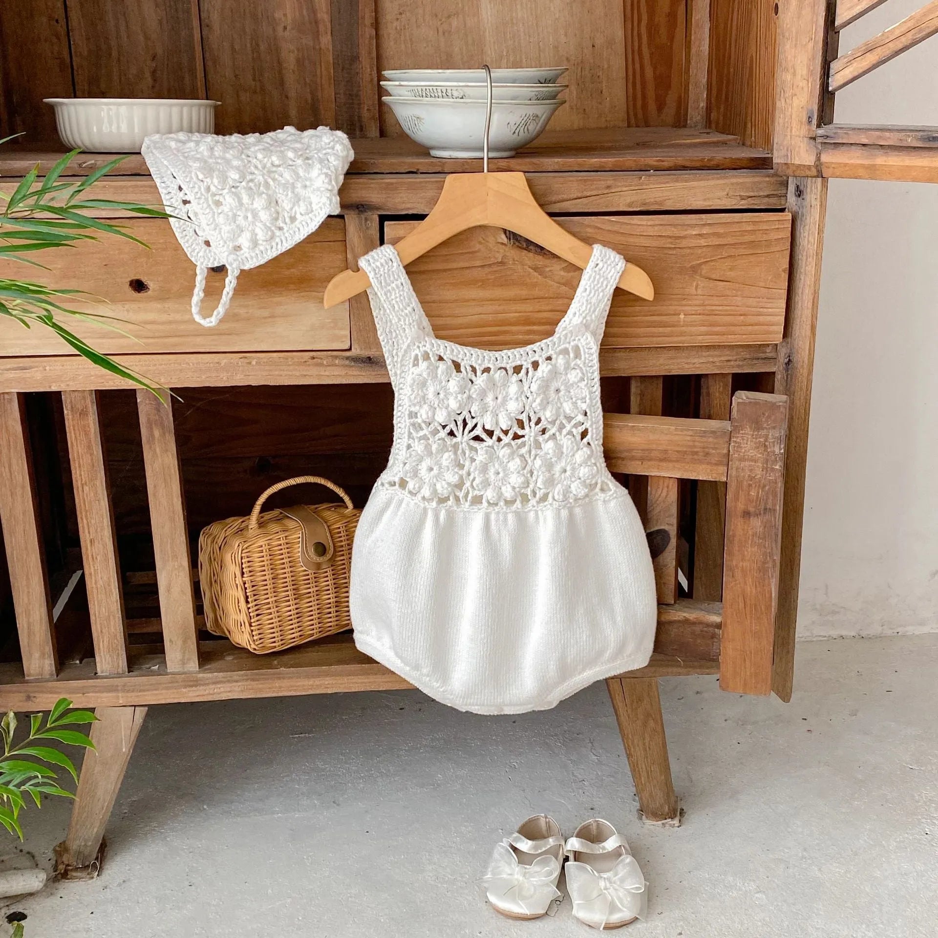 Beige baby romper with flower cutout strap and matching hat on a baby girl