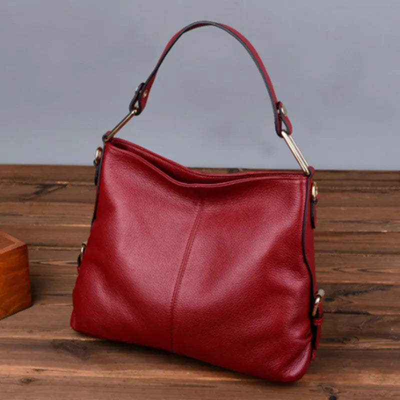 A vertical square-shaped genuine leather crossbody bag in black, showing external sewing lines and a crossbody strap.