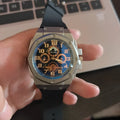 Four-ring Black And Silver Watch on a surface showing round black dial and interlocking metal bracelet