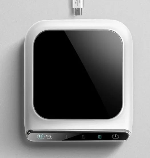 Black USB cup warmer on a desk next to a coffee mug, showing control panel.