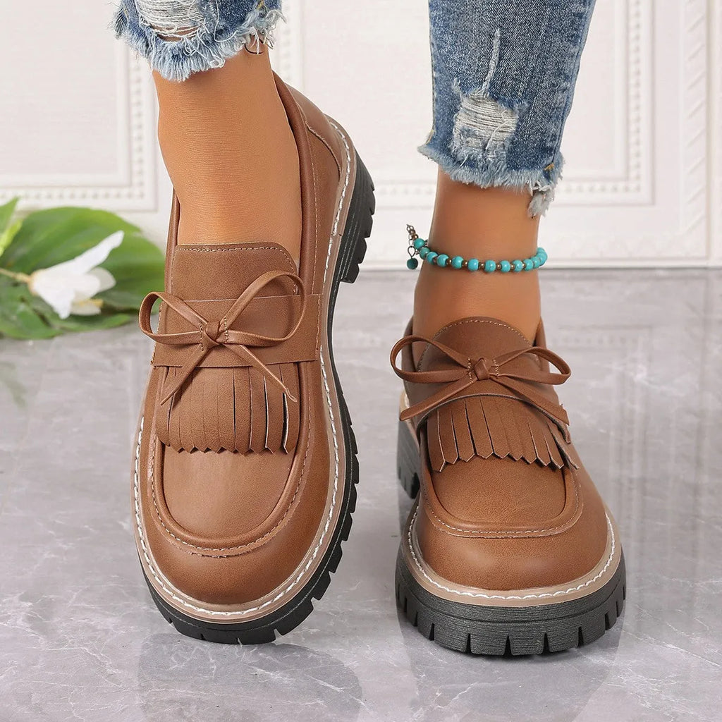 Black plus size women's loafers with a tassel and bowknot detail on a chunky flat rubber sole.