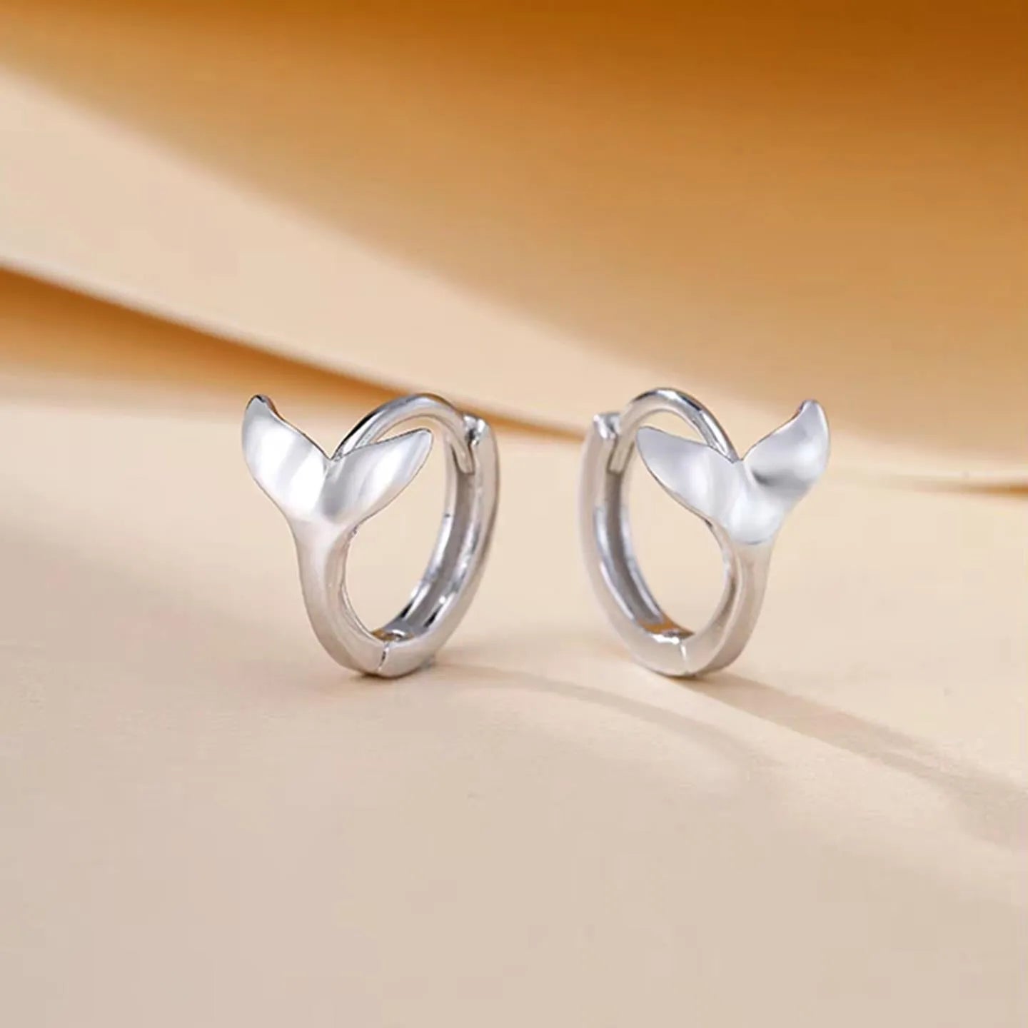 A pair of simple fishtail design earrings with a metallic electroplated finish in either white gold or yellow gold colour.
