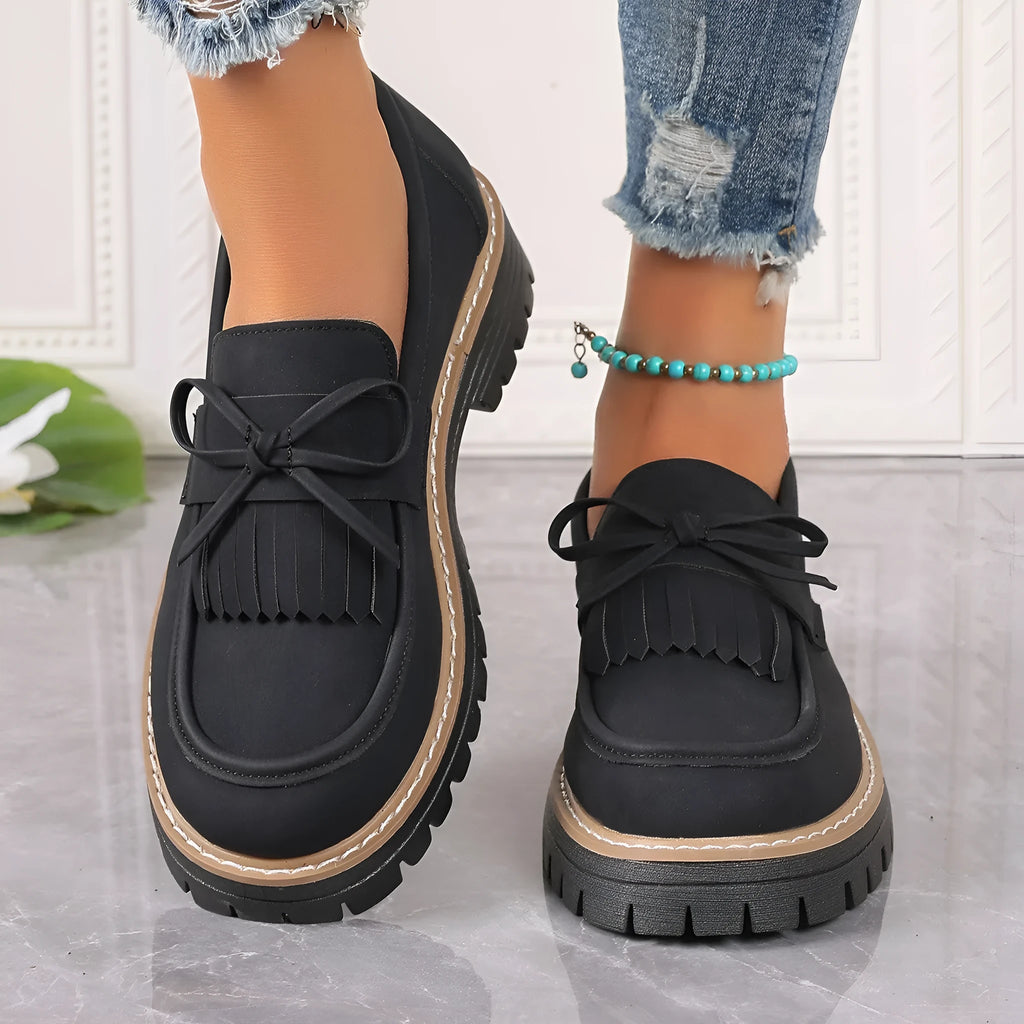 Black plus size women's loafers with a tassel and bowknot detail on a chunky flat rubber sole.