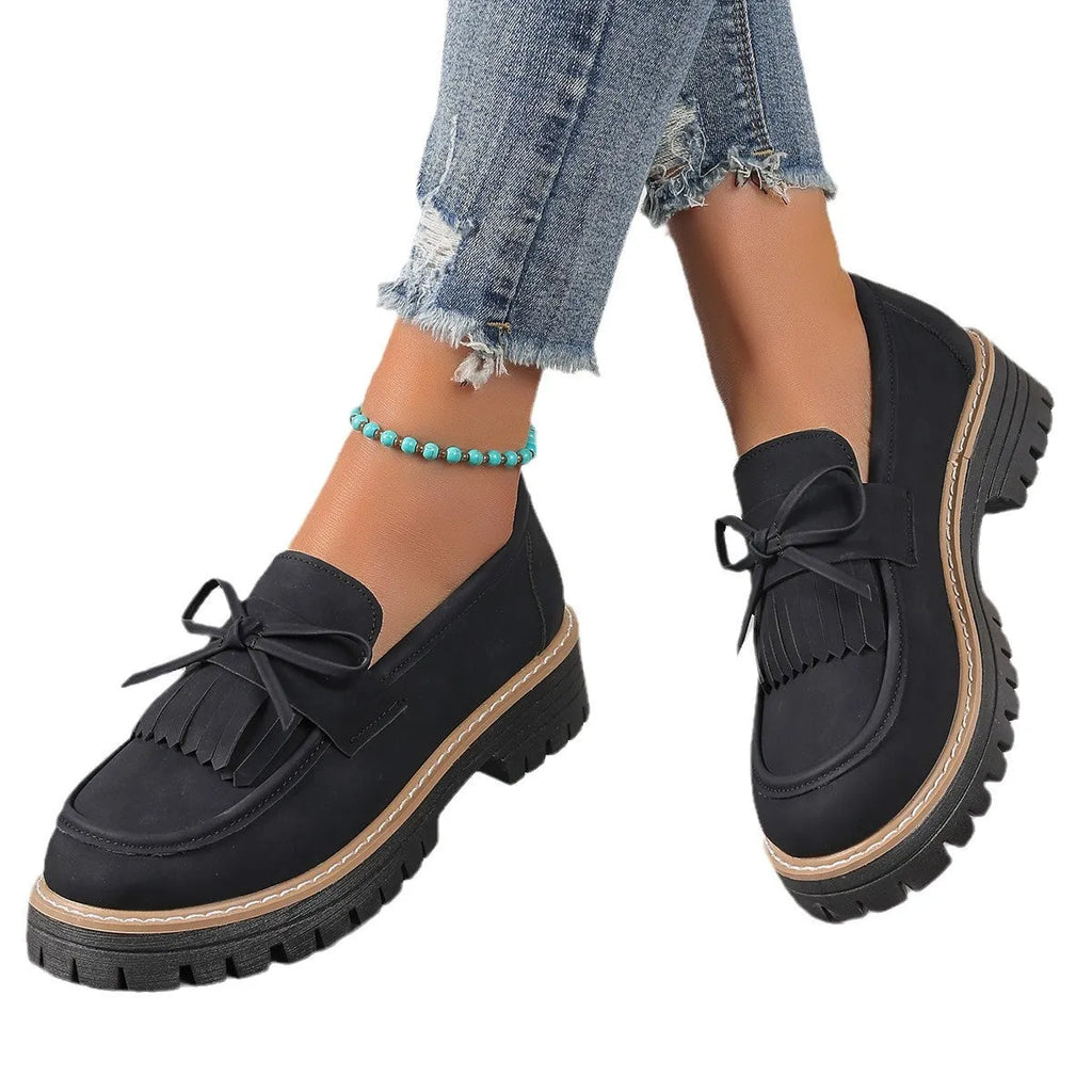 Black plus size women's loafers with a tassel and bowknot detail on a chunky flat rubber sole.
