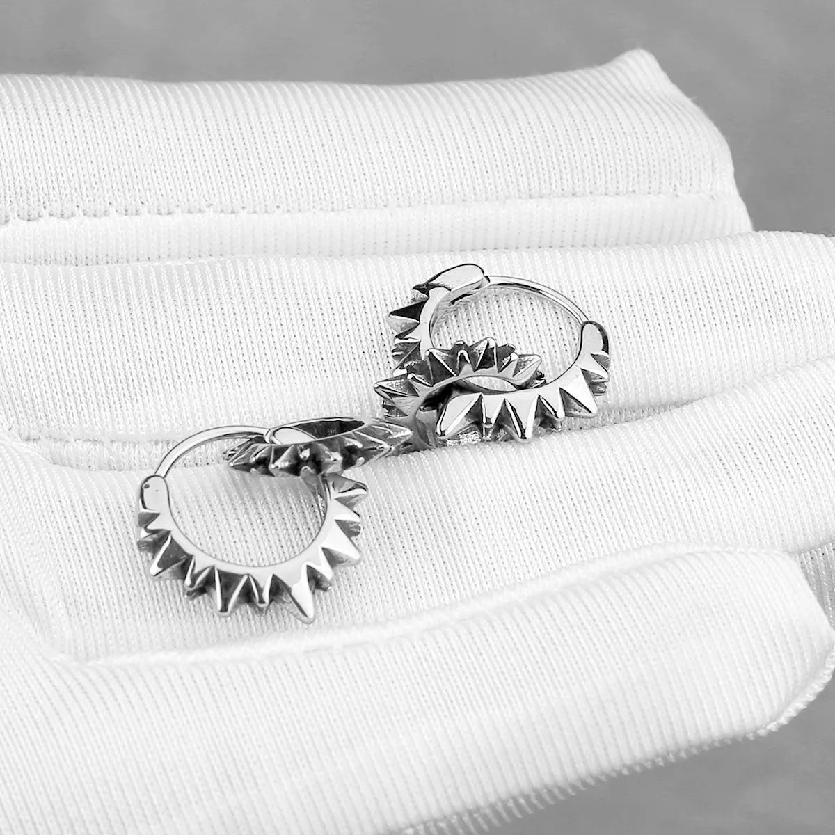 A pair of polished stainless steel round hoop earrings on a simple background.