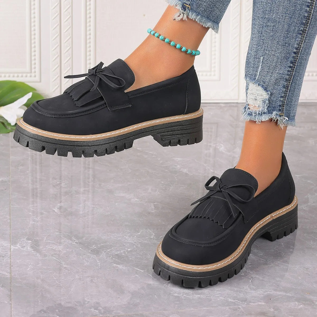 Black plus size women's loafers with a tassel and bowknot detail on a chunky flat rubber sole.