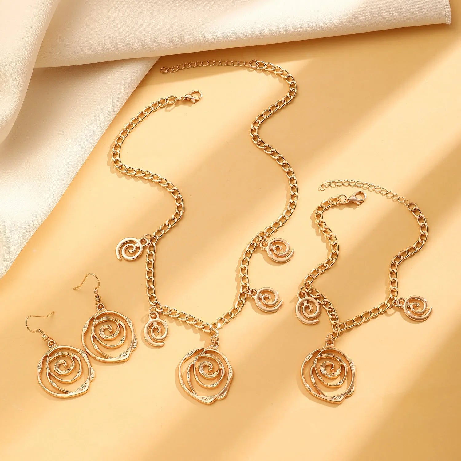 Gold tone spiral donut necklace, bracelet, and earrings set on a white background