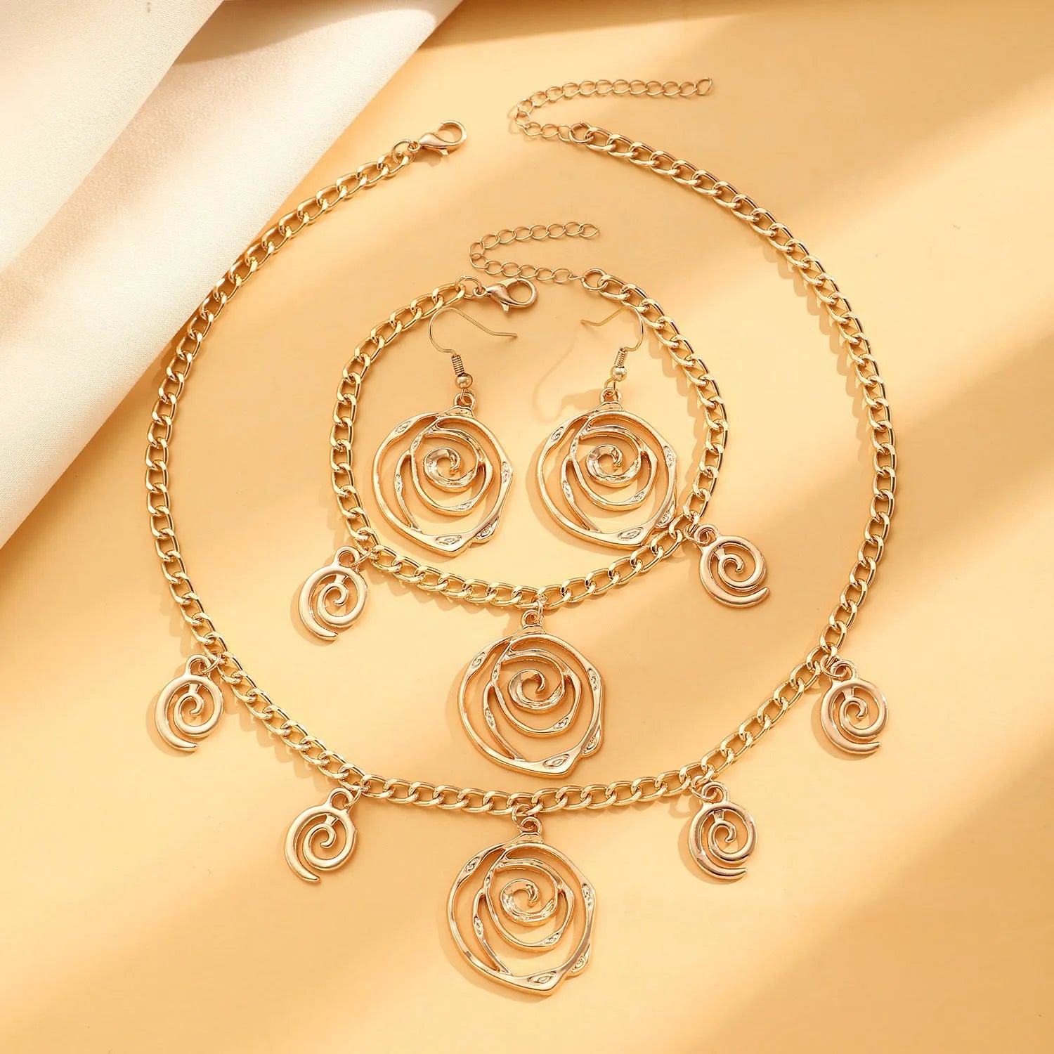 Gold tone spiral donut necklace, bracelet, and earrings set on a white background