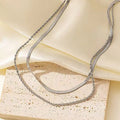 Close-up of a silver geometric double-layer twist pendant on a textured snake bones chain necklace.