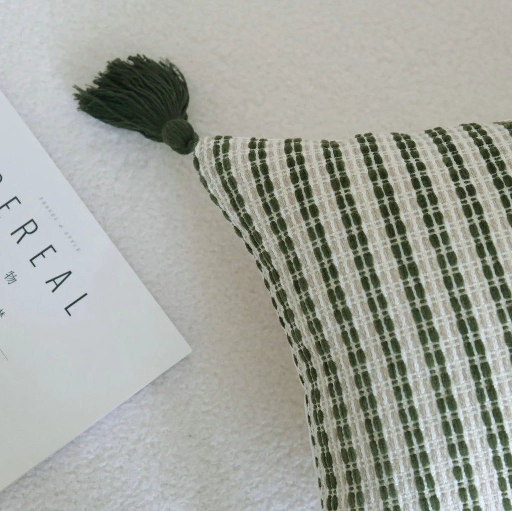 Green cotton and linen hotel pillow with striped or leaf pattern tassel detail on a bed.