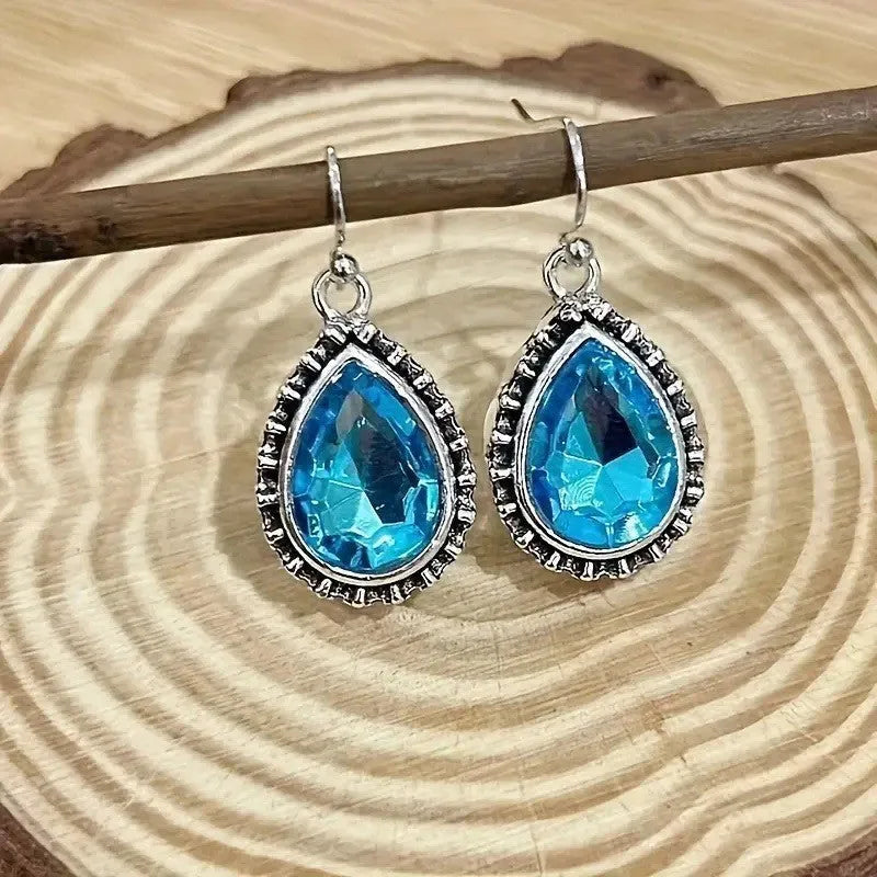Pair of retro drop-shaped silver alloy earrings with blue gem inlay on white background