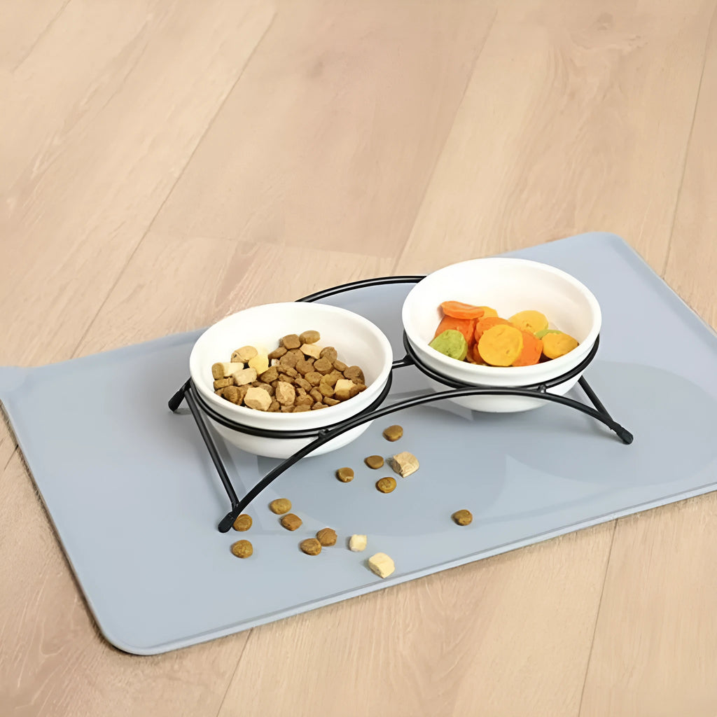 Silicone pet placemat under dog food and water bowls in a grey colour on a wooden floor.