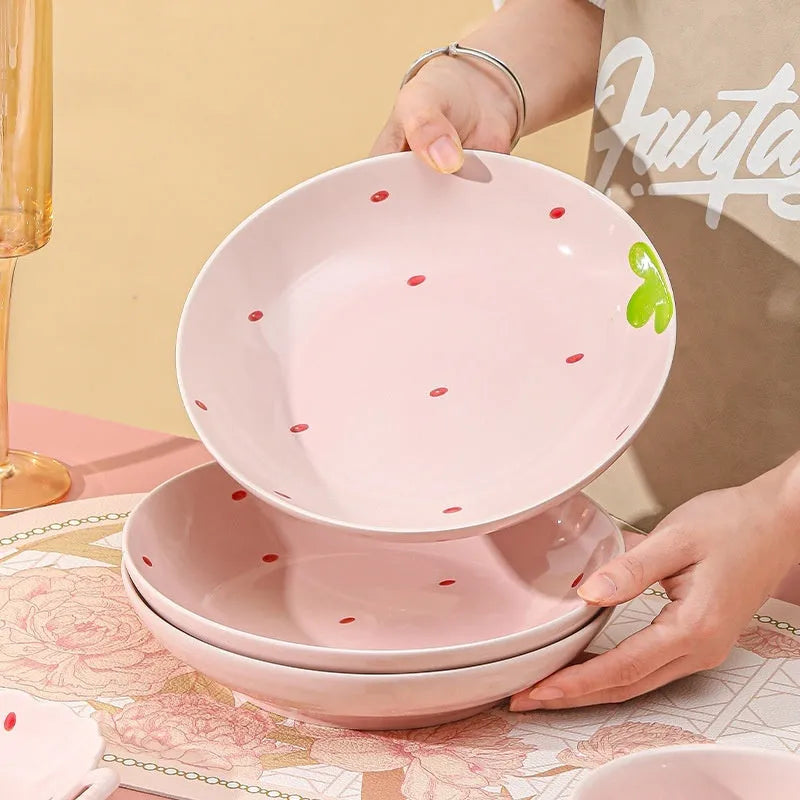 Cute strawberry pattern porcelain dinnerware set with plates, flower bowls, and a twist spoon on a table.