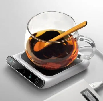 Black USB cup warmer on a desk next to a coffee mug, showing control panel.