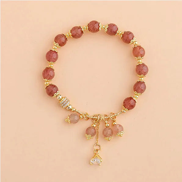 Close-up of a women's pink strawberry quartz crystal bracelet with heart-shaped beads and pearl accents.